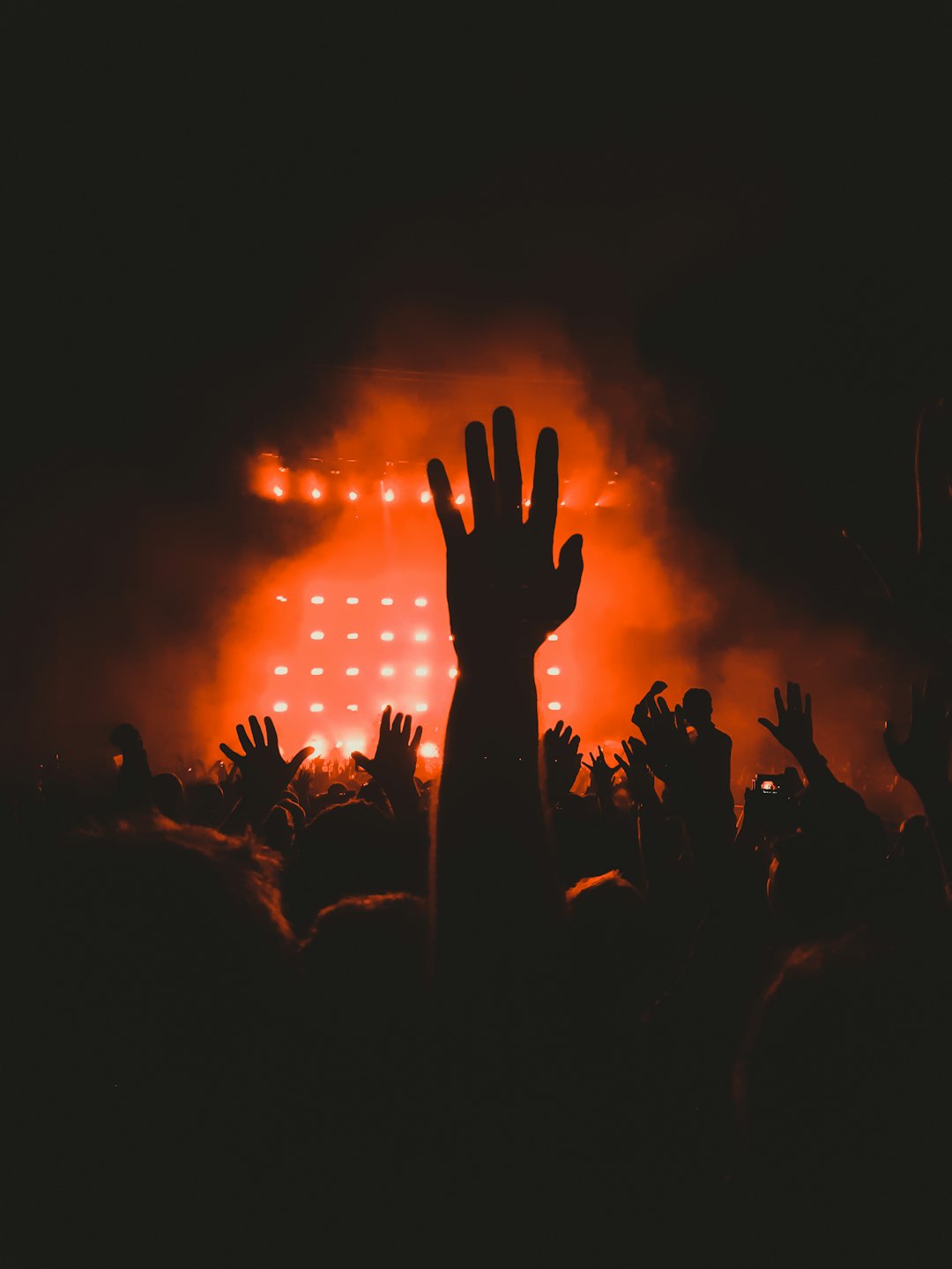 Concert crowd with hands raised in front of orange stage lights.