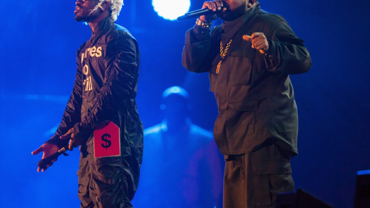 André 3000 and Big Boi of OutKast perform together under blue stage lights.